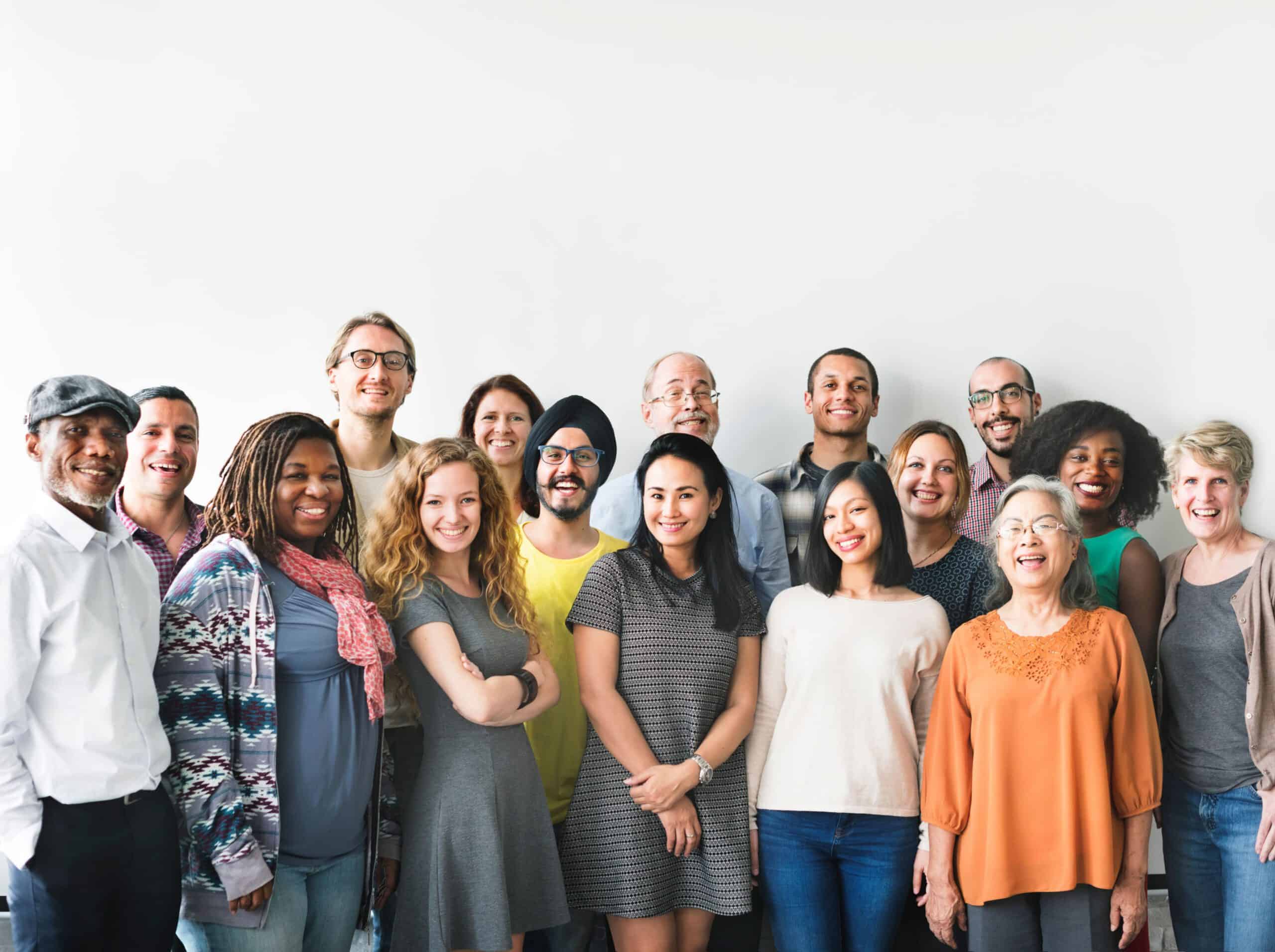 A diverse group stands in two rows against a white background, smiling warmly at the camera, each showing unique personality.