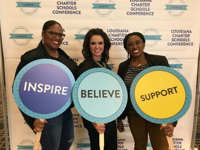 At a Louisiana Charter Schools Conference, three women smile at the camera holding signs reading 