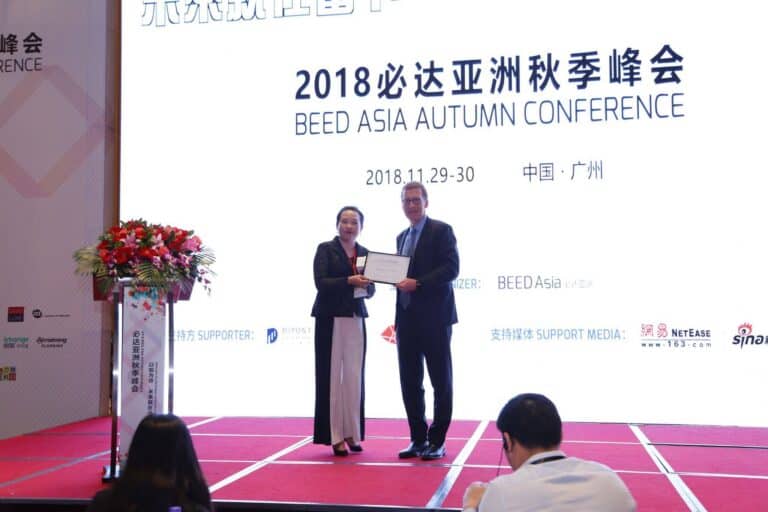 A man and woman on stage hold a certificate at the 2018 BEED Asia Autumn Conference in Guangzhou, China.