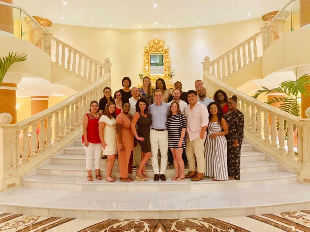 People pose on a grand staircase in a bright, elegant space with marble floors and decorative architectural details.