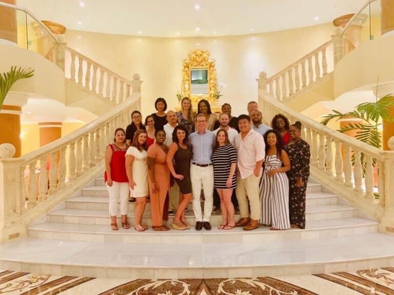 People pose on a grand staircase in a bright, elegant space with marble floors and decorative architectural details.
