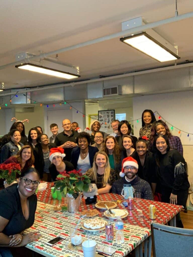 People smiling and posing around a table filled with food and holiday decorations in a festive indoor setting.