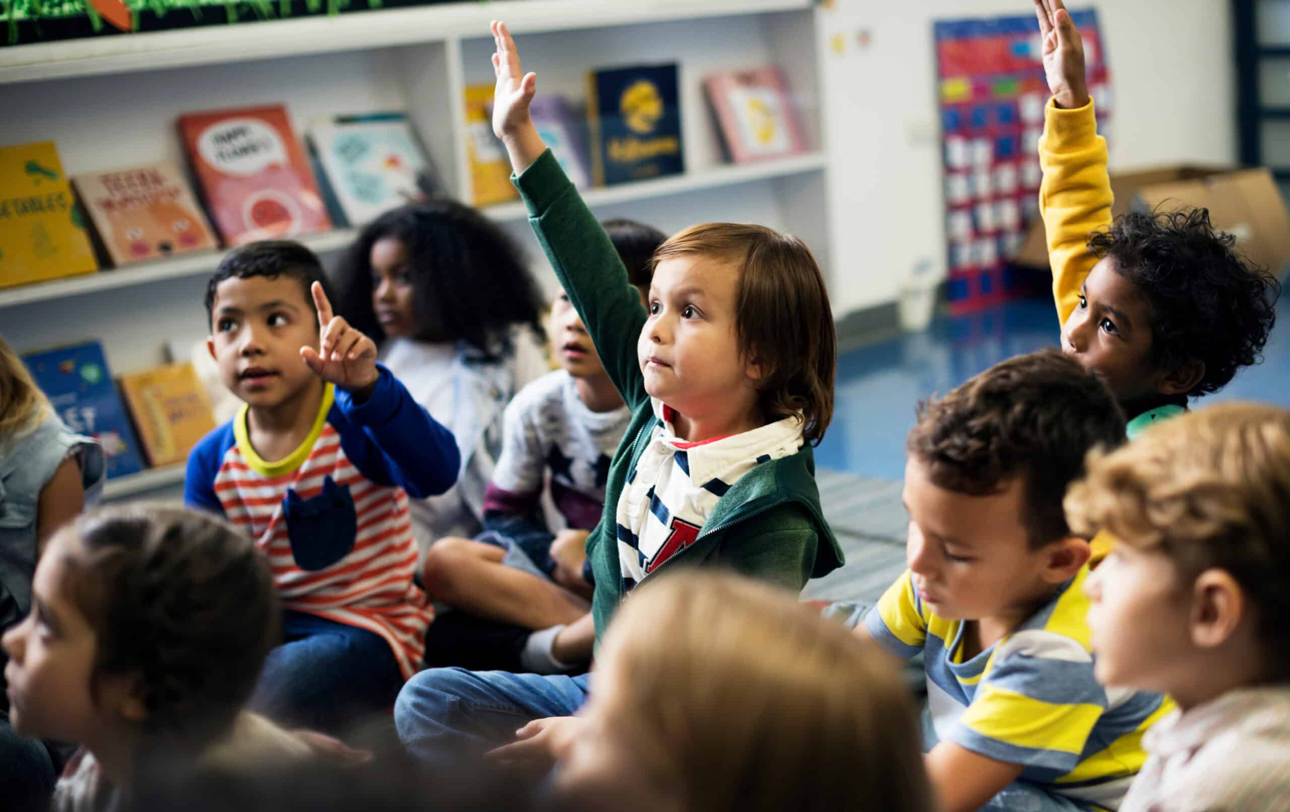A group of kids raise their hands to be called on in a classroom setting