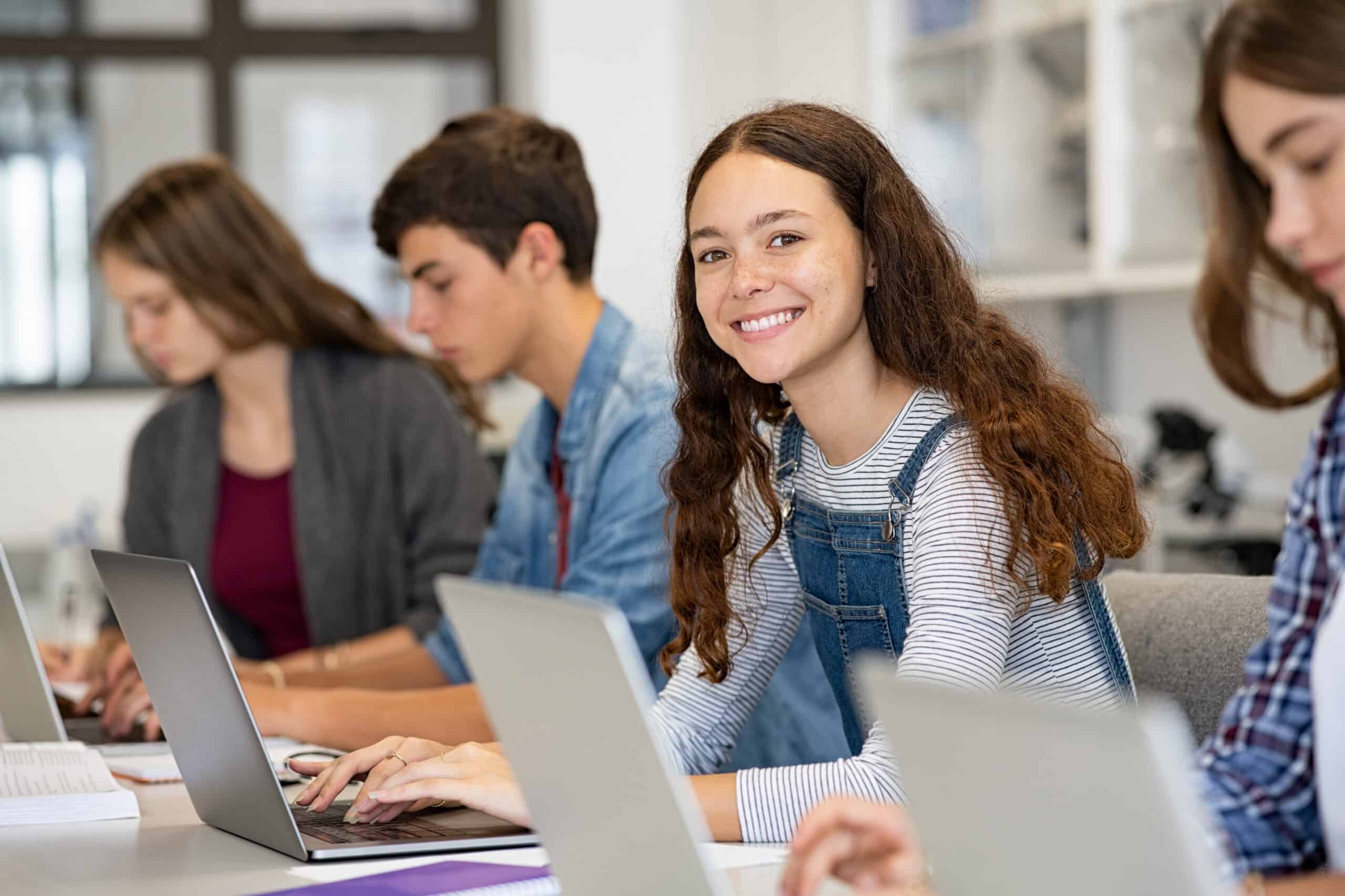 Four students work on laptops at a table, focused on accounting. In the foreground, a girl smiles at the camera.