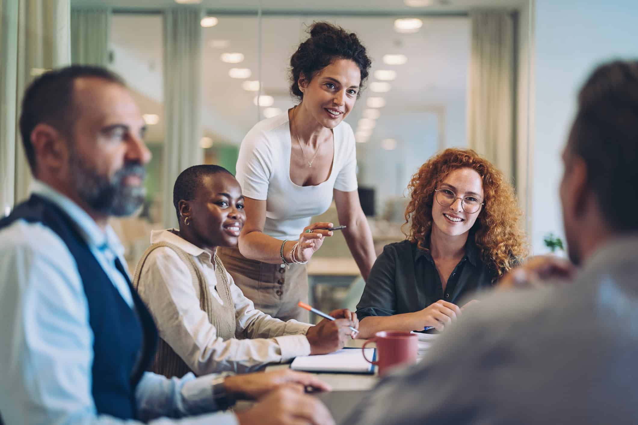 Five people meet in a modern office, with one leading a discussion on financial management at a conference table.
