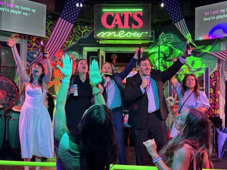 People sing and cheer on stage beneath a neon 