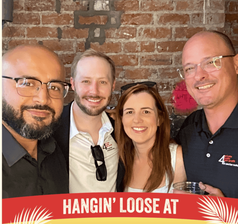 Four people smile together in front of a brick wall, posing for a photo at Lucy’s Retired Surfers Bar & Restaurant.